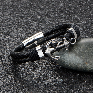 Men's black braided leather bracelet with silver anchor charm on grey stone surface