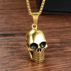 Pendentif crâne gothique en acier titane doré avec chaîne box sur fond de bois sombre
