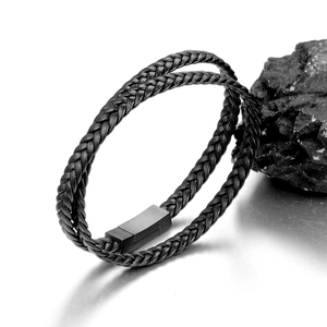 Detail of black braided leather bracelet featuring a matte magnetic metal clasp on dark stone
