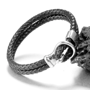 Men's black braided leather bracelet with silver horseshoe buckle on black rock