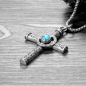 Macro shot of retro stainless steel cross pendant with engraved scrolls and blue turquoise