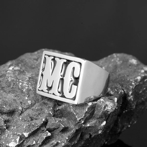 Macro shot of men's vintage stainless steel square ring with MC engraving on dark rock