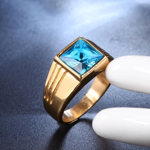 Macro shot of gold men's ring with square blue gemstone and side engraved details