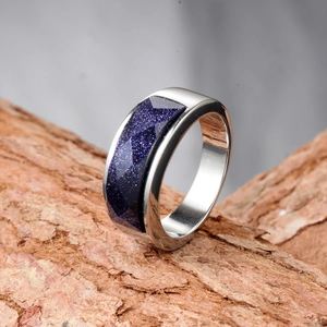 Polished stainless steel ring with faceted blue sandstone inlay on natural bark background