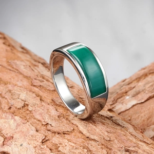 Polished stainless steel ring with rectangular green stone on a natural bark base