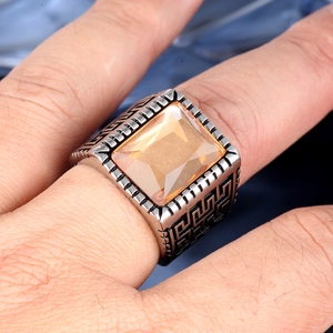 Macro detail of men's stainless steel ring with square amber gem and Greek key patterns