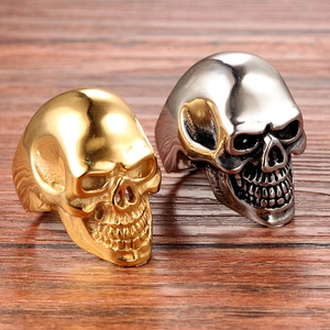 Gothic skull rings in gold and silver steel finishes on a dark wood background