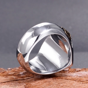Polished silver men's stainless steel wide ring with gold relief on a rustic wood base