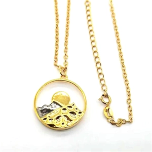 Detailed view of golden mountain and sun relief pendant on a delicate cable chain