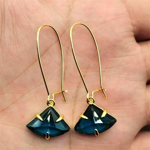 Détail de boucles d'oreilles dorées en éventail avec pampilles en cristal bleu sur main