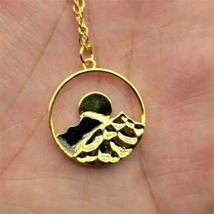 Macro view of a gold-plated mountain and sun relief pendant on a fine link chain