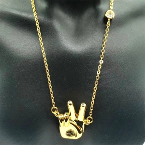 Detail of gold-plated peace sign hand pendant with a small sparkling zircon stone