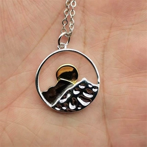 Close-up of circular mountain pendant with gold and silver dual-tone plating on hand