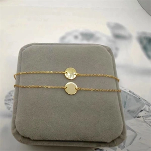 Macro shot of gold-plated silver round disc charm bracelet on a grey jewelry display