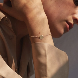 Polished gold round tag minimalist silver bracelet shown on model wrist under soft light