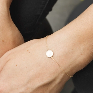 Close-up of a minimalist golden bracelet with a round tag pendant on a wrist