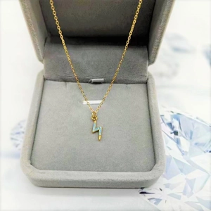 Collier doré avec pendentif éclair et pierres bleues sur un présentoir gris