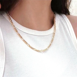 Gros plan d'un collier chaîne Figaro doré porté par un mannequin sur un haut blanc