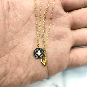 Detail of gold circular pendant with black micro-inlay and star pattern on a thin chain