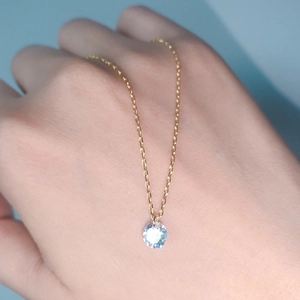 Detailed view of single cubic zirconia pendant on a thin gold chain worn on the hand