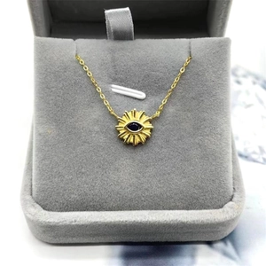Close-up of golden sunburst evil eye pendant with blue center on grey velvet