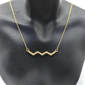 Detail of a wavy gold necklace pendant encrusted with white crystals on a black mannequin
