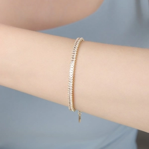 Dettaglio di un bracciale tennis dorato con zirconi rettangolari sul polso di una modella