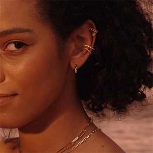 Détail de boucles d'oreilles goutte dorées avec gemme verte et ear cuffs étoile sur modèle