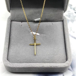 Close-up of minimalist gold cross necklace presented in a grey velvet jewelry box