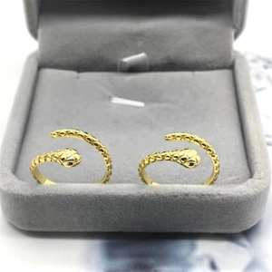 Macro detail of two gold snake rings with scale texture and black stone eyes in a box