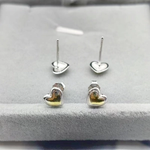 Detail view of heart-shaped silver stud earrings with high-polished finish and secure backs