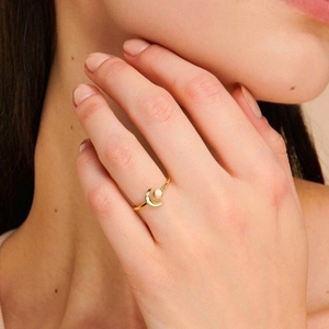 Detail of elegant gold crescent moon ring with white opal stone worn on model finger