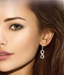 Close-up of infinity symbol silver drop earrings with shimmering crystals on model's ear