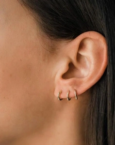 Close-up of three minimalist gold sterling silver geometric hoop earrings on a model ear