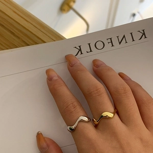 Close-up of stacked gold and silver wavy rings with a polished mirror finish on a hand