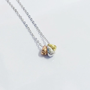 Close-up of three-tone bean-shaped pendants in silver, rose gold, and gold on a fine chain