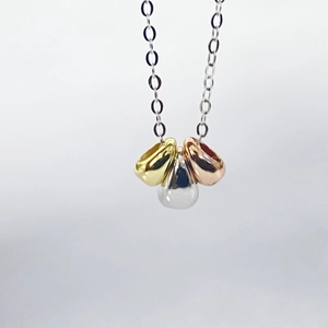 Close-up of tricolor teardrop pendants in gold, silver, and rose gold on a fine silver chain