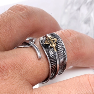 Detailed close-up of retro stainless steel feather ring with golden cross emblem