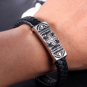 Macro detail of braided leather bracelet featuring a silver vintage cross relief charm