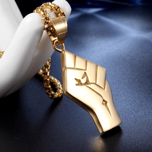 Detail of golden stainless steel fist pendant with textured finish on a jewelry stand