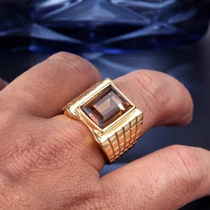 Macro shot of men's gold ring featuring a large rectangular brown gemstone and grid texture