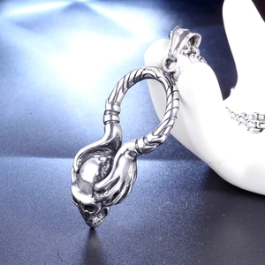 Détail d'un pendentif crâne vintage en acier inoxydable avec mains squelettiques gothiques