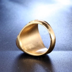 Macro side view of polished gold stainless steel signet ring on textured dark background