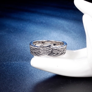 Vintage stainless steel cross ring with intricate feather patterns on ceramic display