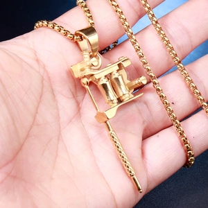 Gros plan d'un pendentif machine à tatouer doré avec une chaîne box sur une main
