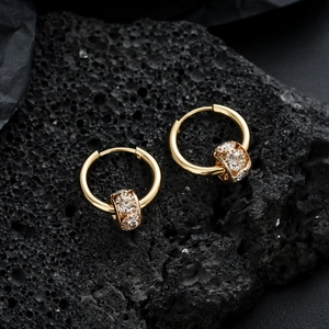 Elegant gold hoop earrings with zircon studded cylinder pendant on black lava rock
