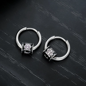 Unisex silver hoop earrings with black enamel star charm on textured wood background
