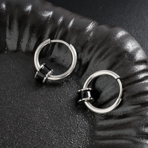 Boucles d'oreilles créoles en acier argenté avec pendentif noir sur plateau sombre