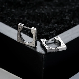 Silver square huggie earrings with geometric patterns on a black stone background