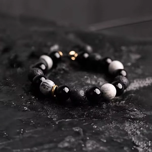 Men's obsidian and volcanic stone beaded bracelet with golden spacers on dark rock